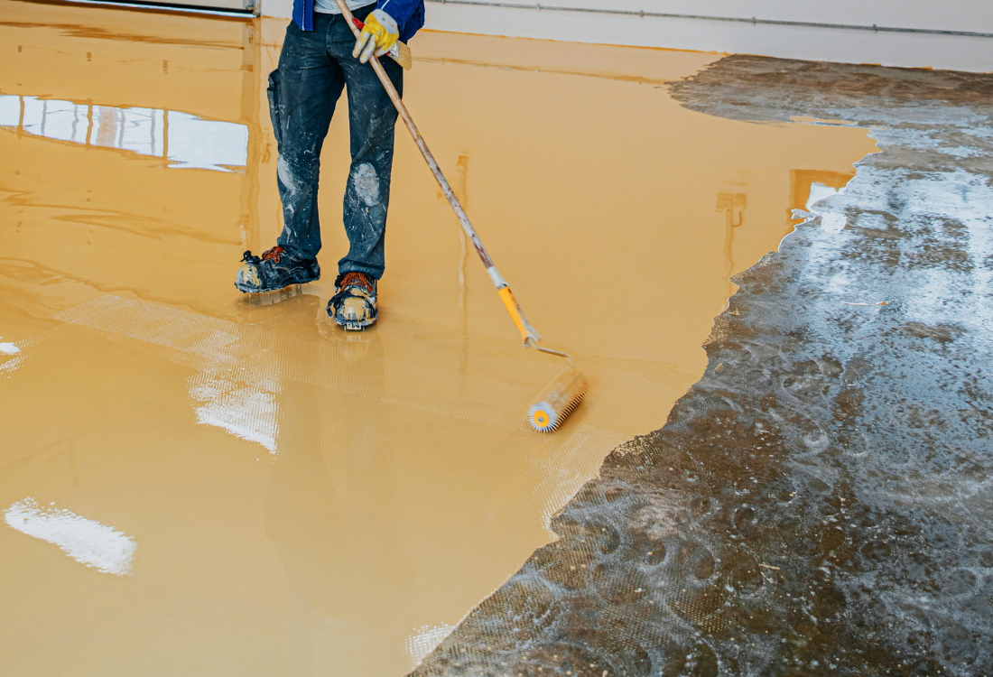 Worker applying resin coating on damaged industrial floor to repair cracks and prevent costly long-term damage.